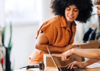 Two small business owners reviewing online orders and inventory together in a clothing shop.