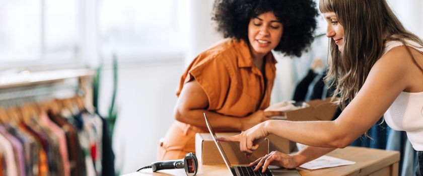 Two small business owners reviewing online orders and inventory together in a clothing shop.